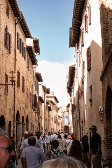 Belebte Altstadtstraße mit historischen Steinhäusern in San Gimignano
